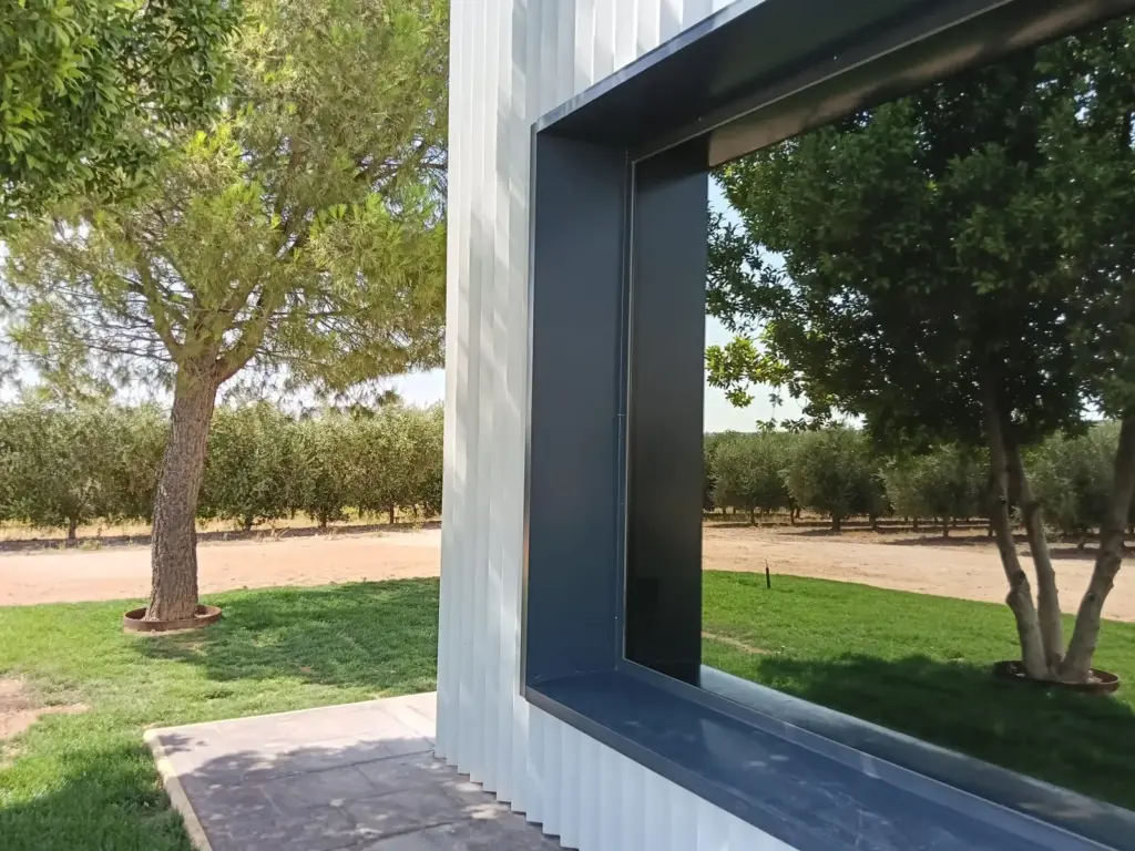 Exterior de la sala de catas de Pagos de Aherca con ventanal enmarcando el olivar y los pinos de la finca